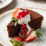 a slice of chocolate olive oil cake topped with greek yogurt whip and berries on a plate.