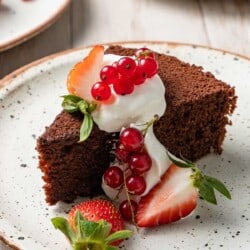 a slice of chocolate olive oil cake topped with greek yogurt whip and berries on a plate.