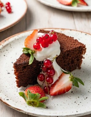 a slice of chocolate olive oil cake topped with greek yogurt whip and berries on a plate.