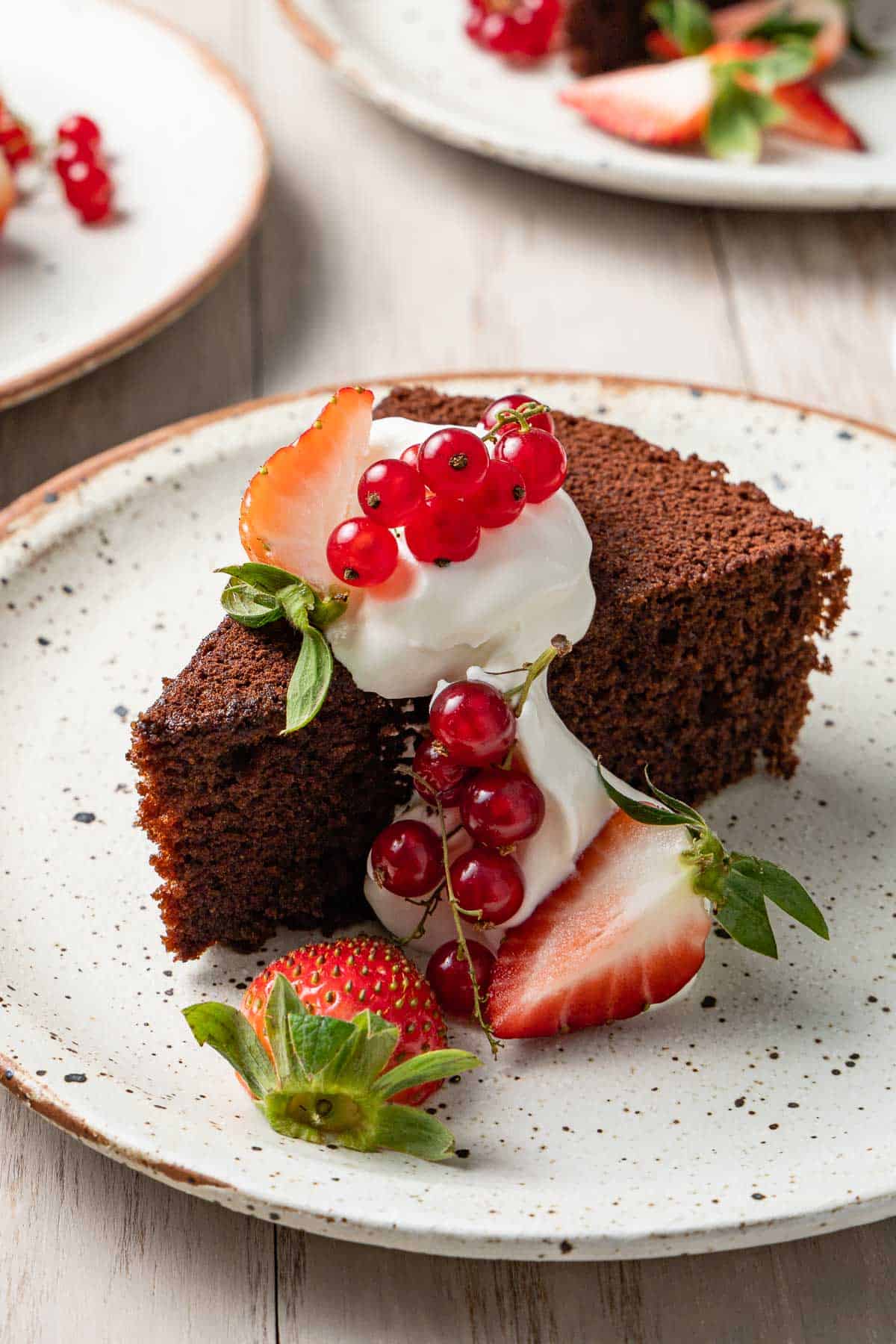 a slice of chocolate olive oil cake topped with greek yogurt whip and berries on a plate.