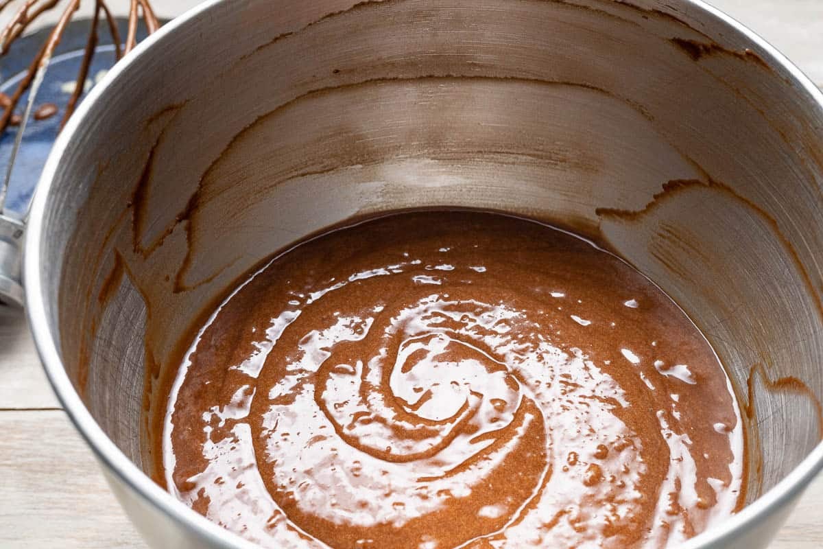 chocolate olive oil cake batter in the bowl of a stand mixer next to a whisk attachment.