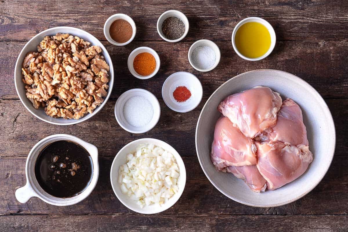 ingredients for fesenjan (persian pomegranate and walnut chicken stew) including walnuts, olive oil, diced onion, bone in chicken thighs, turmeric, cinnamon, saffron, pomegranate molasses, sugar, sea salt and pepper.