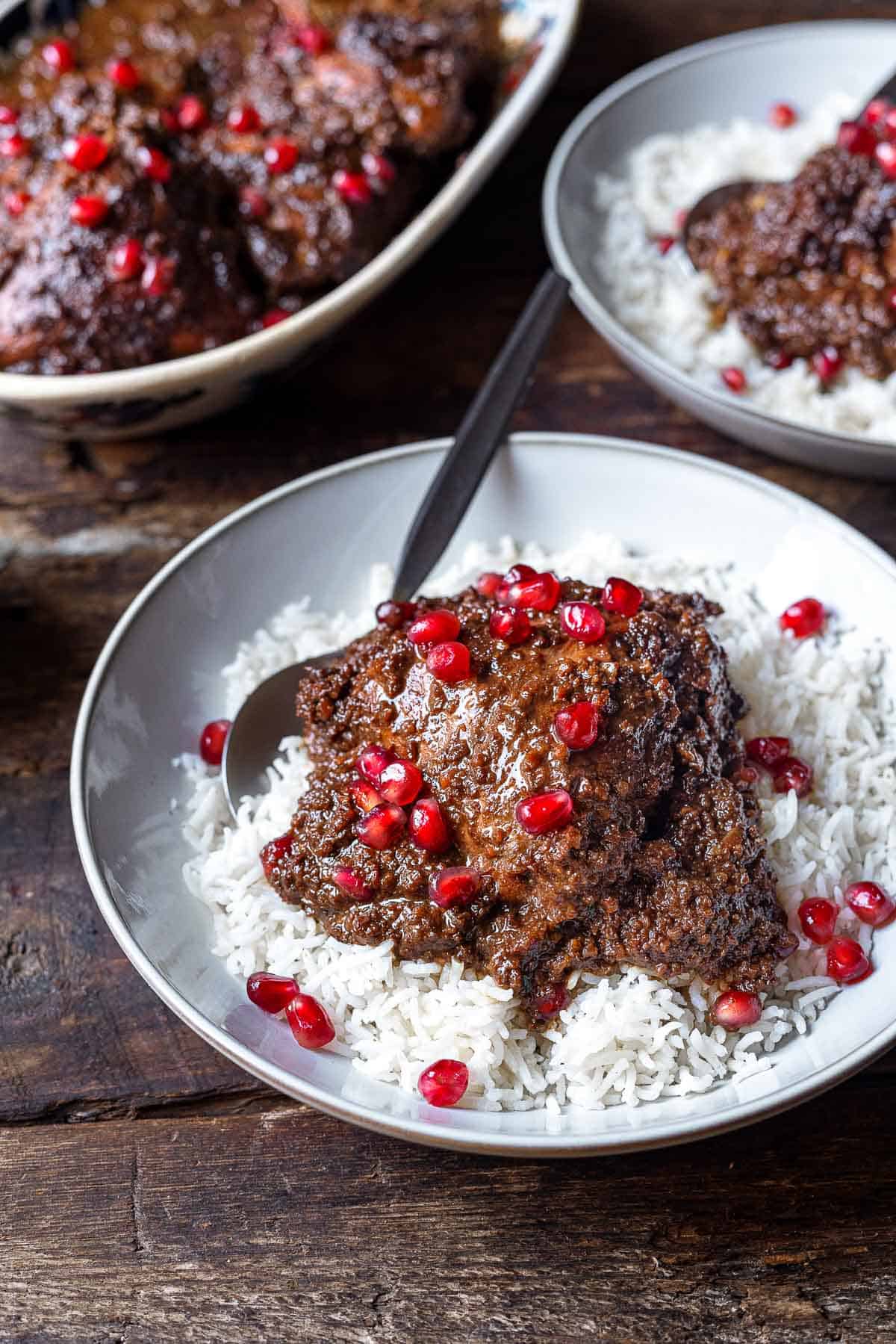 Fesenjan (persian pomegranate and walnut chicken stew) over rice in a bowl with a spoon.