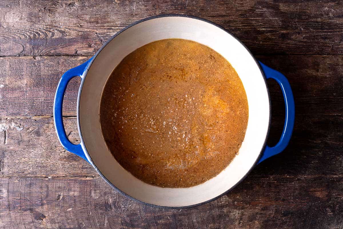 chicken thighs covered with water and spices, simmering in a dutch oven.