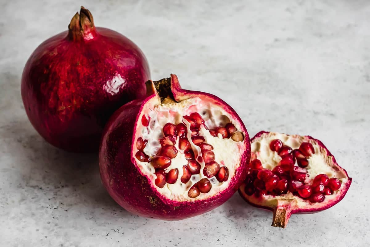 two pomegranates, one whole and one partially opened.