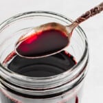 a spoonful of pomegranate molasses resting over a jar full of pomegranate molasses.