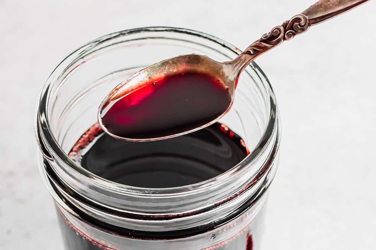 a spoonful of pomegranate molasses resting over a jar full of pomegranate molasses.