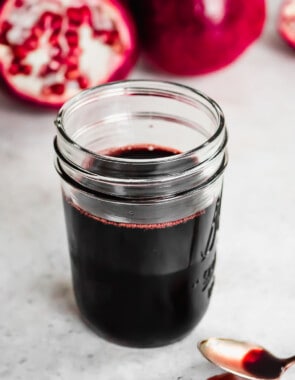 a jar of pomegranate molasses next to a spoon with some pomegranate molasses.