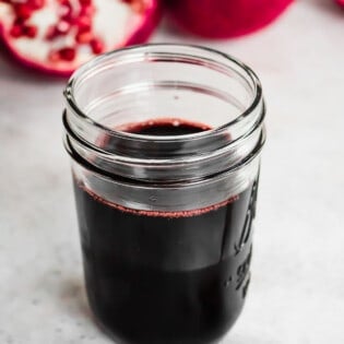 a jar of pomegranate molasses next to a spoon with some pomegranate molasses.