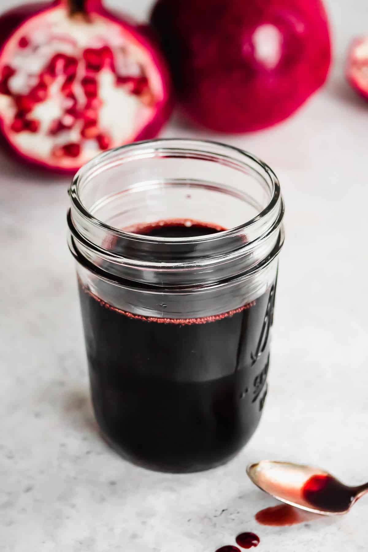 a jar of pomegranate molasses next to a spoon with some pomegranate molasses.