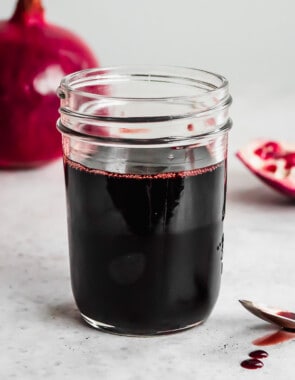 a jar of pomegranate molasses next to a spoon with some pomegranate molasses.
