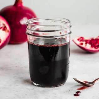 a jar of pomegranate molasses next to a spoon with some pomegranate molasses.