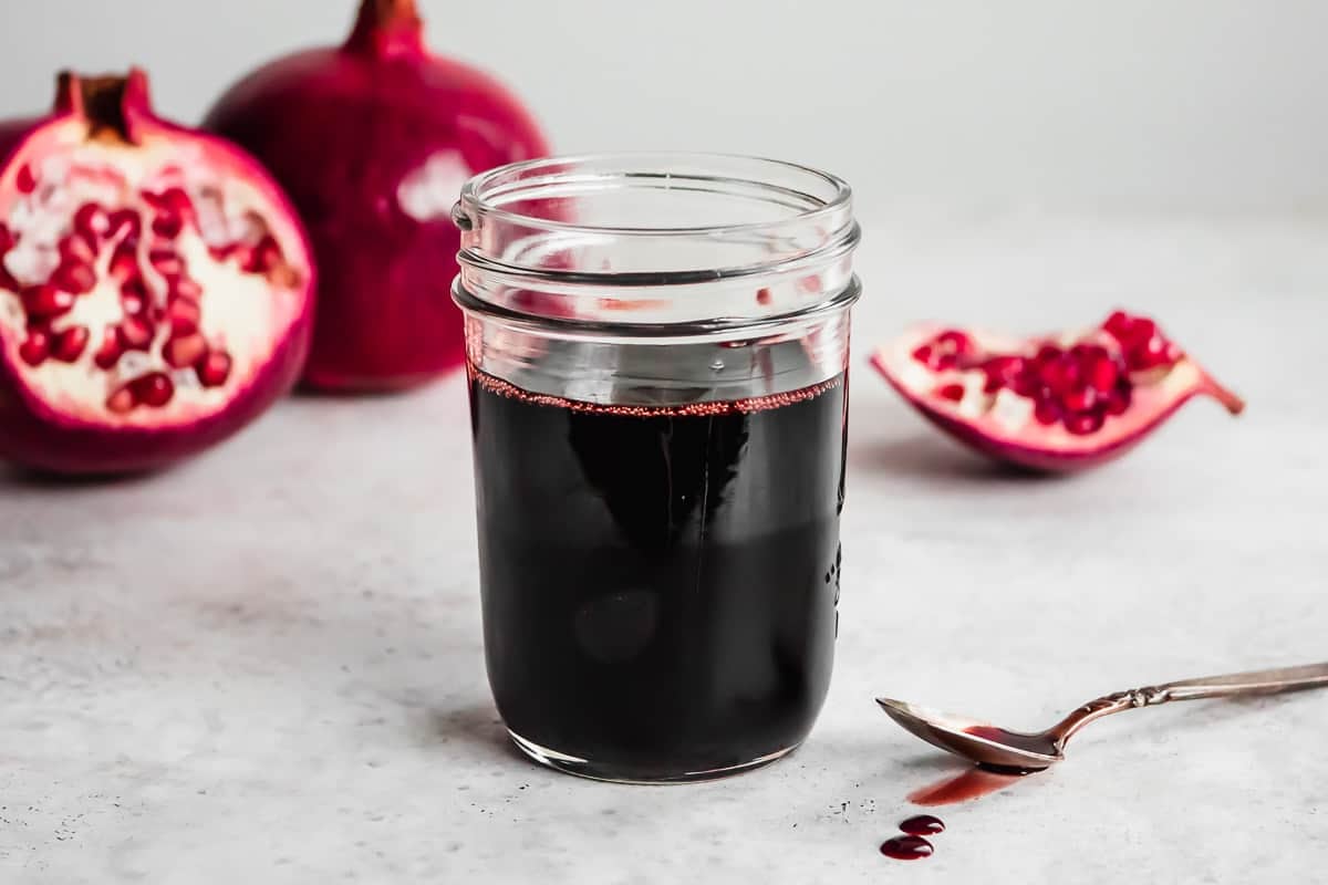 a jar of pomegranate molasses next to a spoon with some pomegranate molasses.