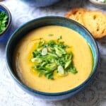 close up of a bowl of potato soup topped with green onions and parsley next to two pieces of toasted bread.