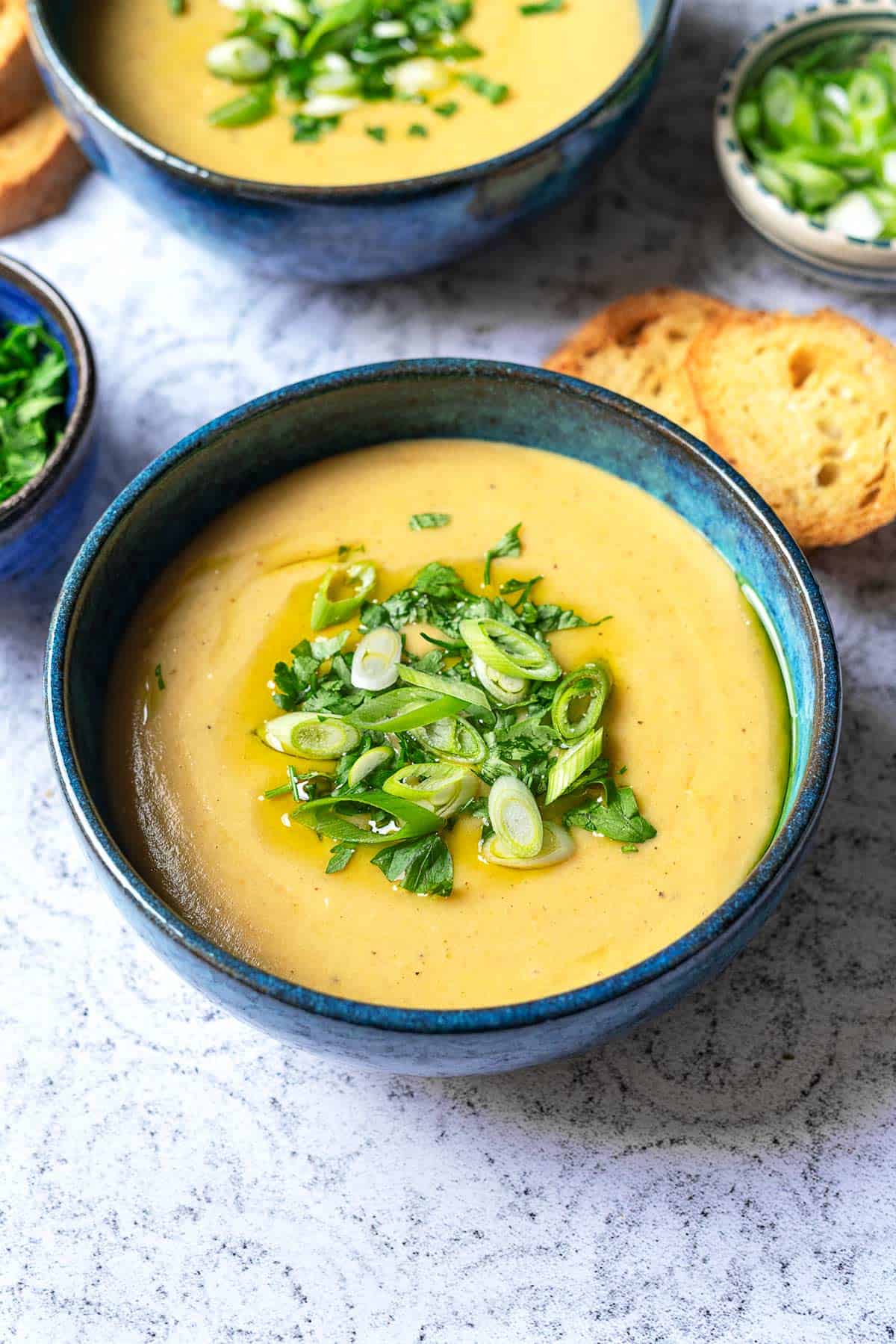 close up of a bowl of potato soup topped with green onions and parsley next to two pieces of toasted bread.