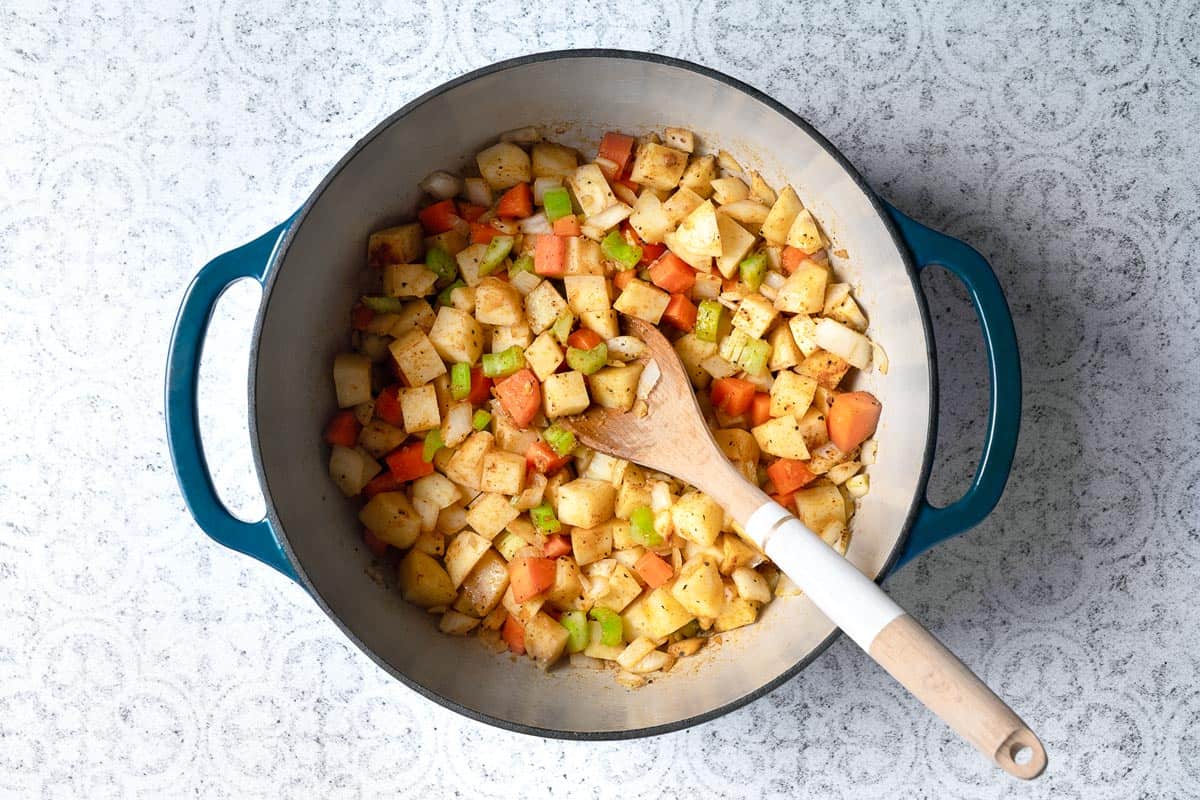 diced onions, carrots, potatoes and celery in a dutch oven with a wooden spoon.