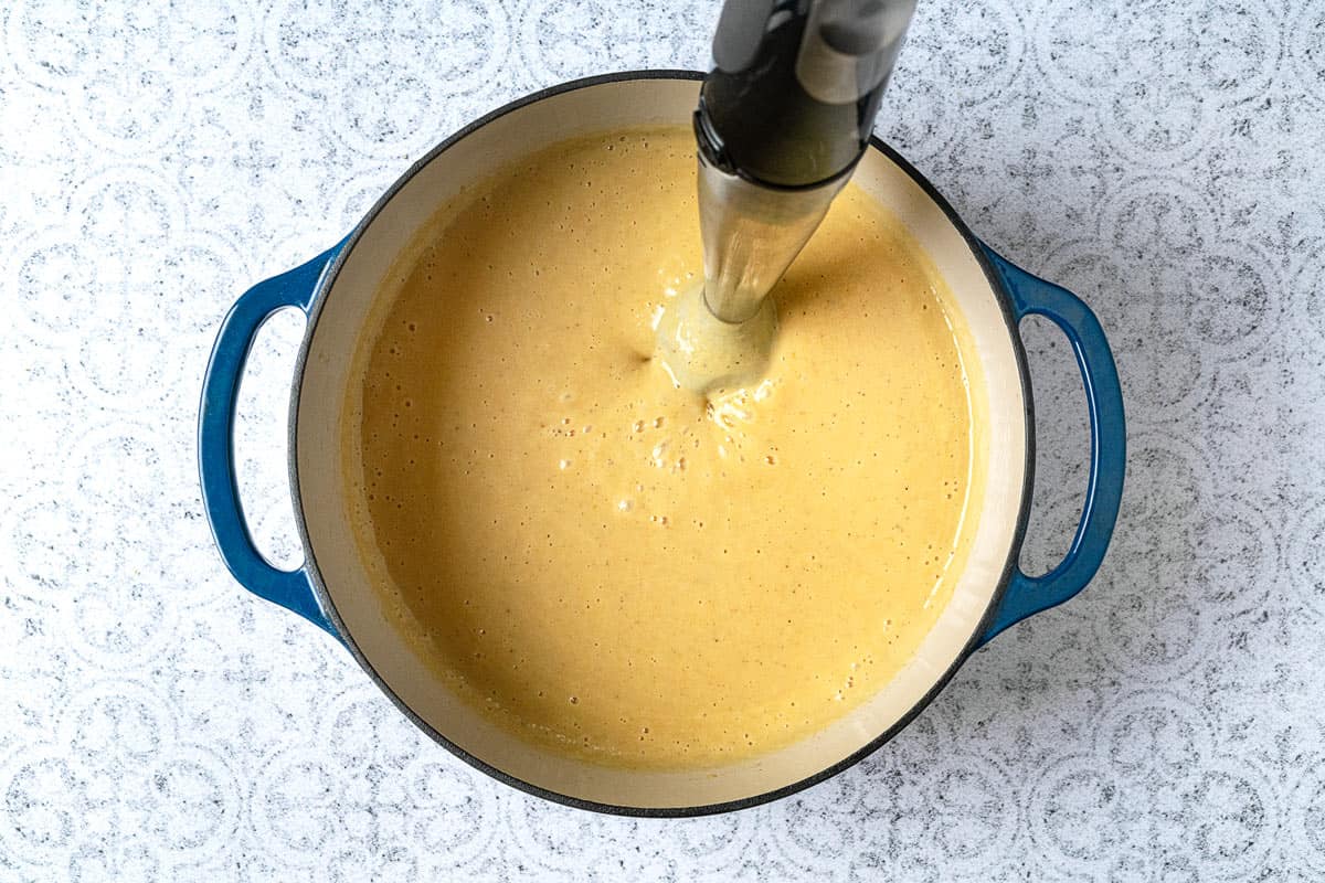 potato soup in a dutch oven being blended with an immersion blender.