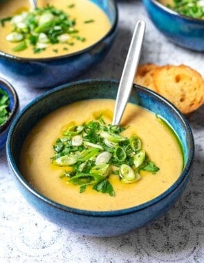 a close up of a bowl of potato soup with a spoon topped with green onions and parsley.