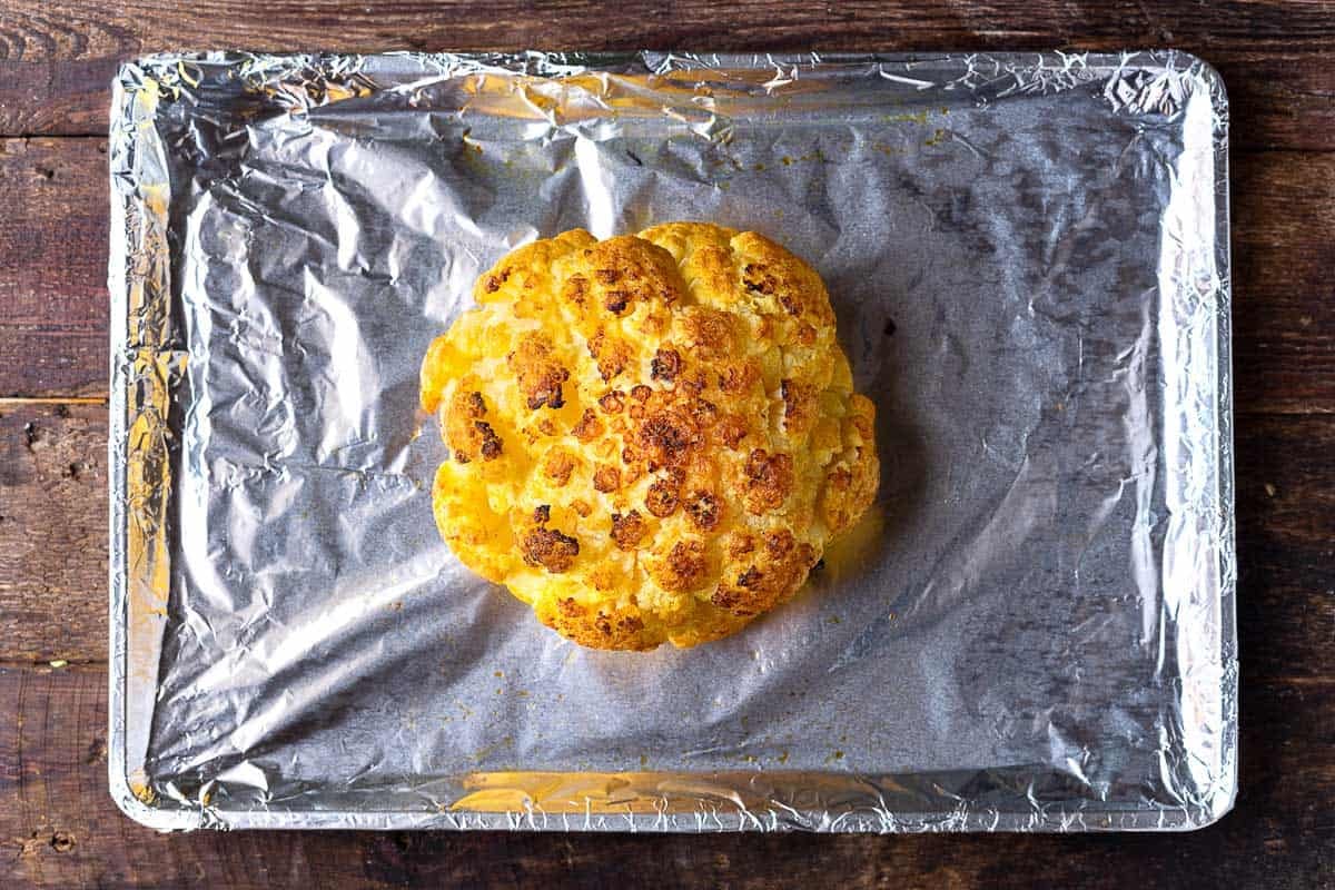 a head of roasted cauliflower on a baking sheet line with aluminum foil.