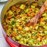 vegan lentil vegetable stew in a dutch oven with a wooden spoon, next to a bowl of chopped parsley.