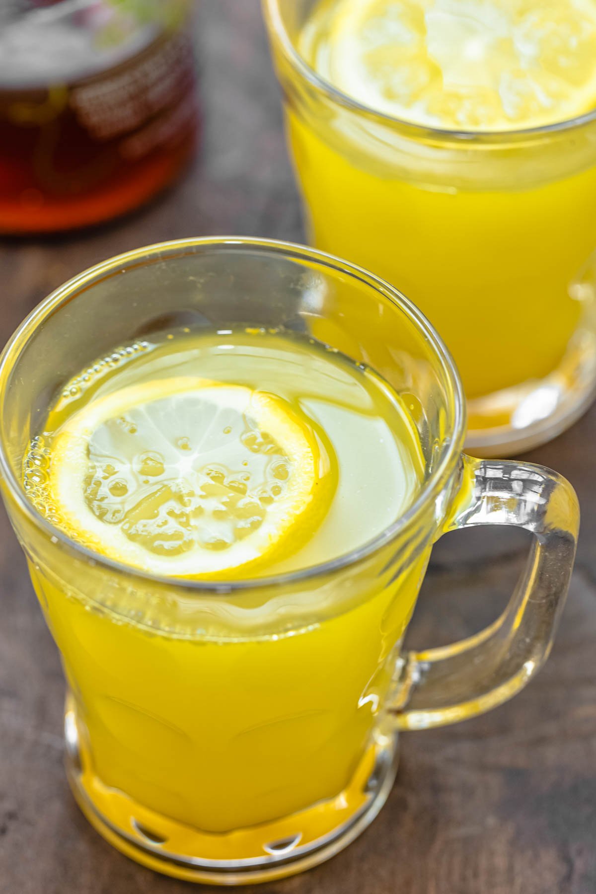 two glass mugs of lemon ginger tea with a sliced lemon in each mug.