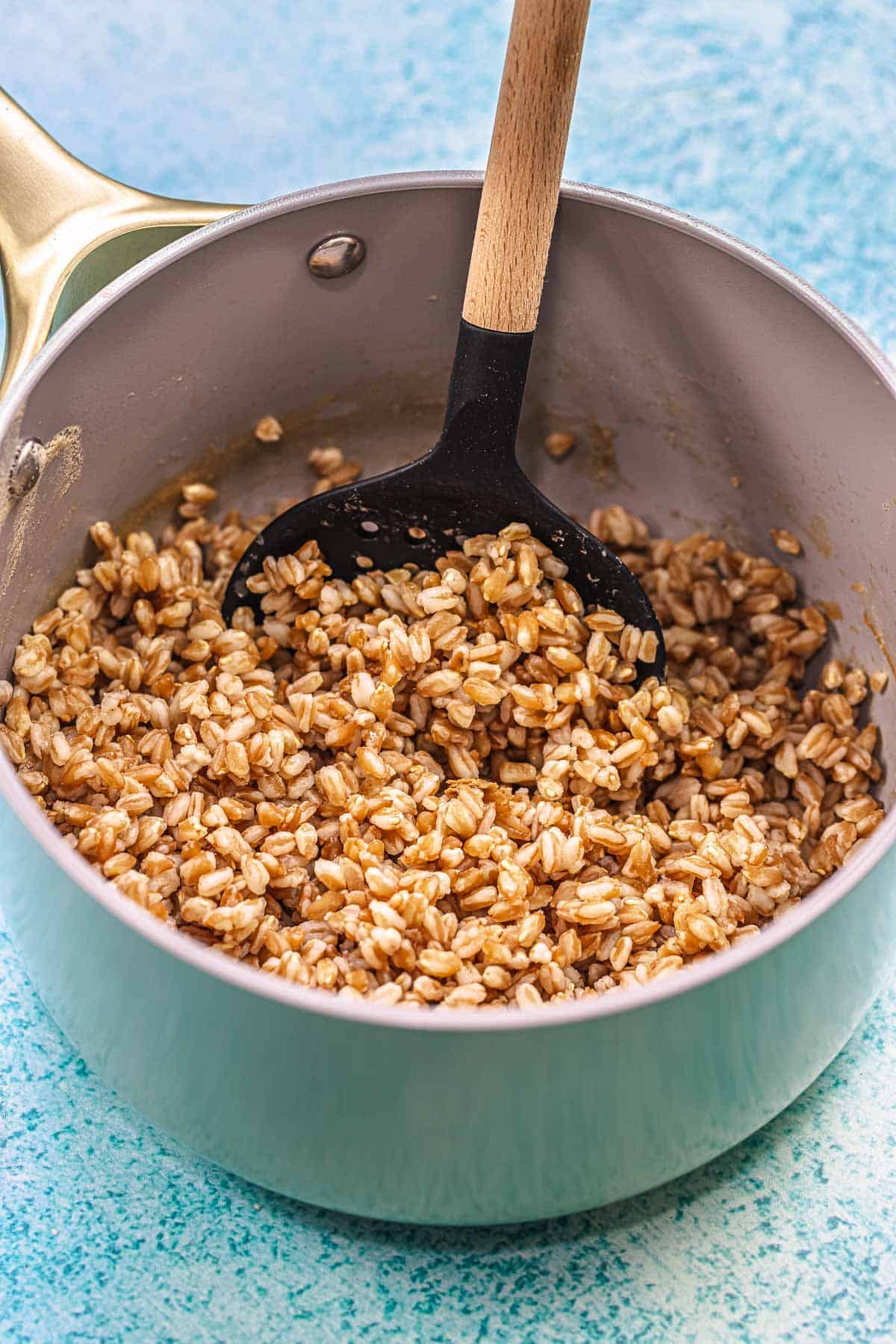 cooked farro in a sauce pan being stirred with a slotted spoon.