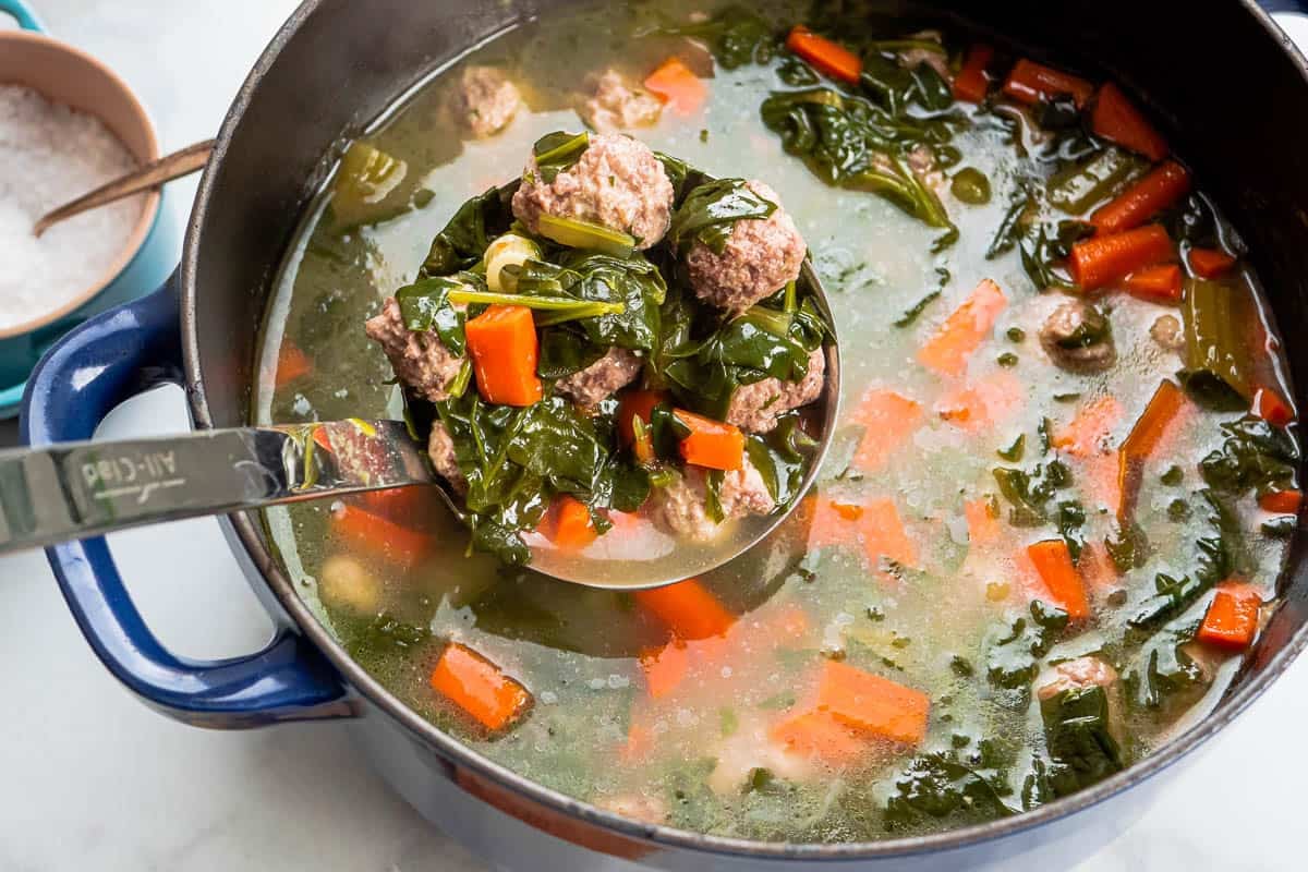Italian wedding soup being ladled out of a dutch oven.