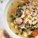 a bowl of italian wedding soup next to a piece of crusty bread.
