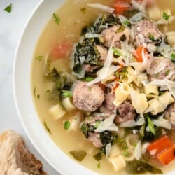 a bowl of italian wedding soup next to a piece of crusty bread.