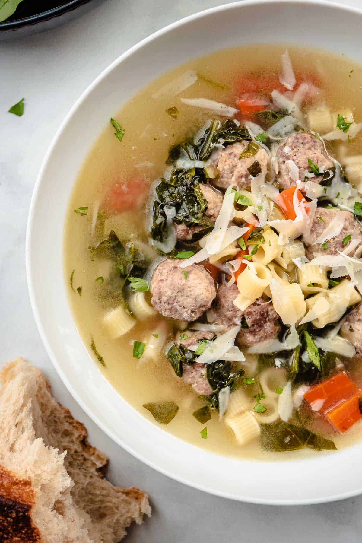 a bowl of italian wedding soup next to a piece of crusty bread.