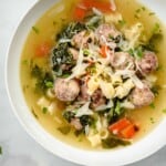 a bowl of italian wedding soup next to a piece of crusty bread.