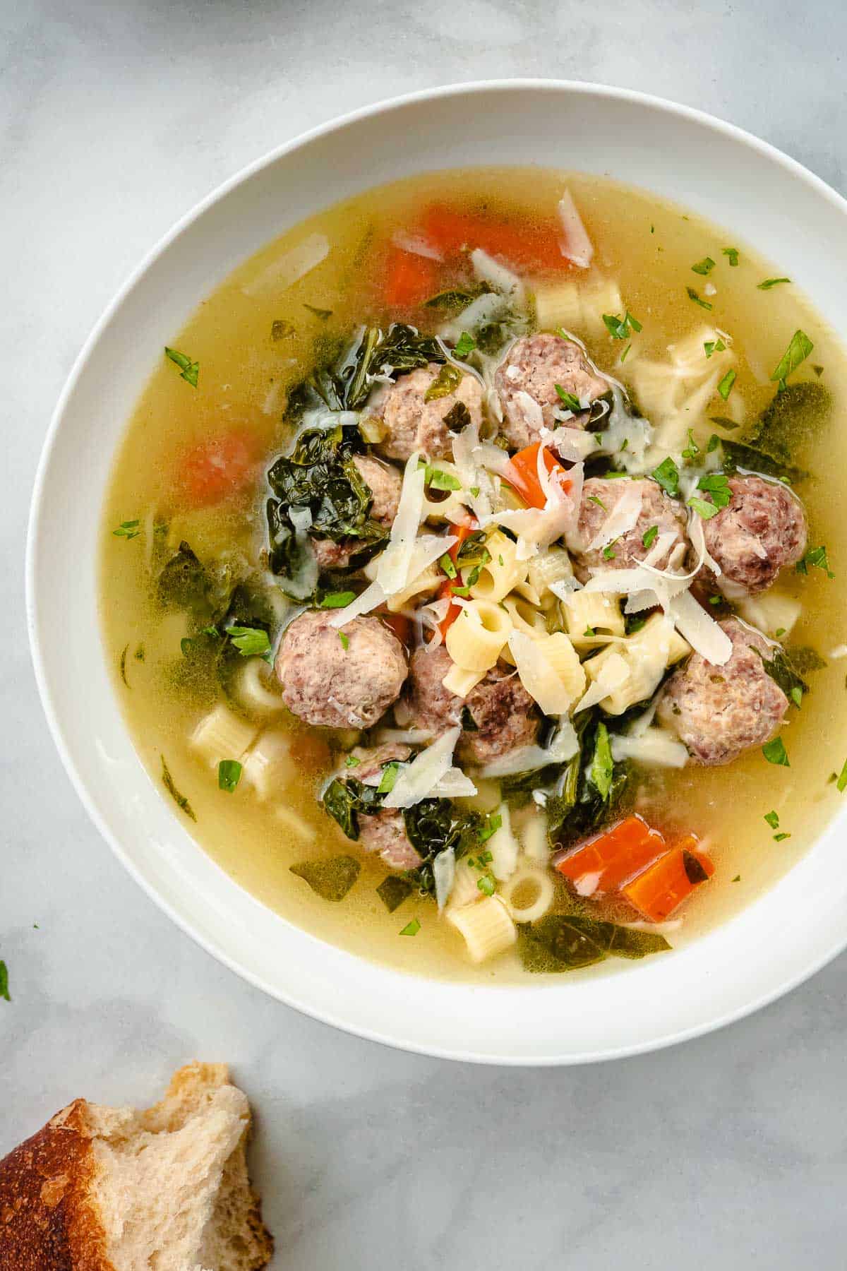 a bowl of italian wedding soup next to a piece of crusty bread.