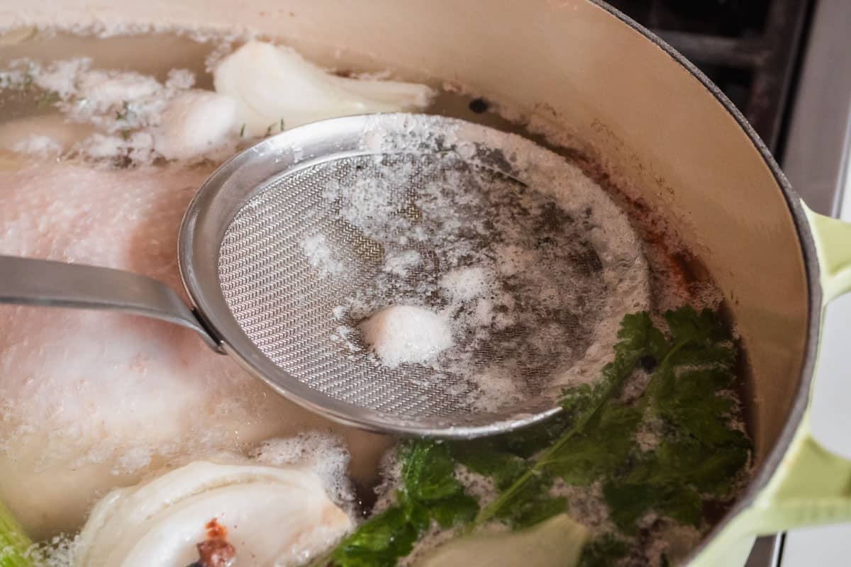 foam being skimmed from a pot of chicken broth cooking on the stove.