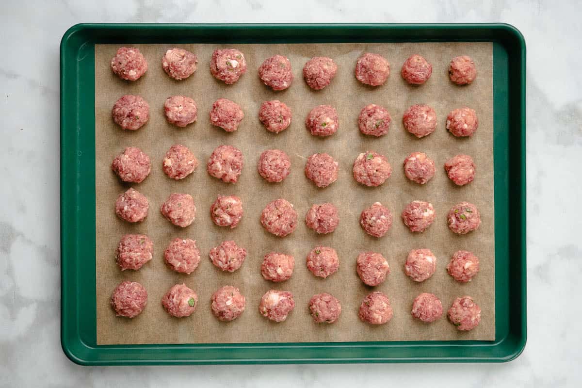 42 raw meatballs on a parchment lined baking sheet.