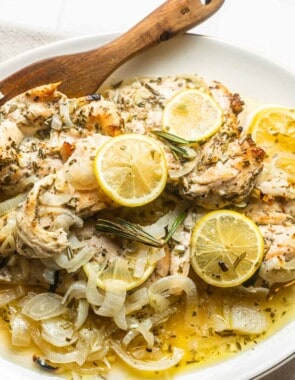 lemon rosemary chicken topped with lemon slices on a plate with a wooden spoon.