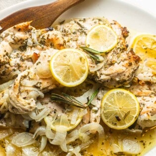 lemon rosemary chicken topped with lemon slices on a plate with a wooden spoon.