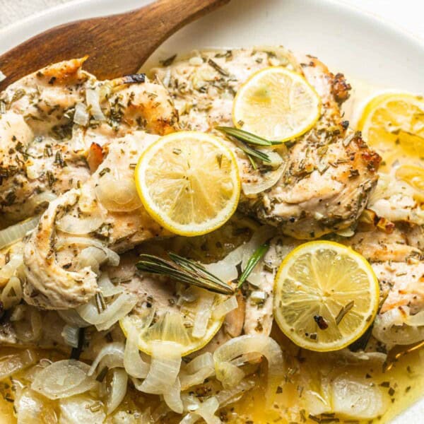 lemon rosemary chicken topped with lemon slices on a plate with a wooden spoon.