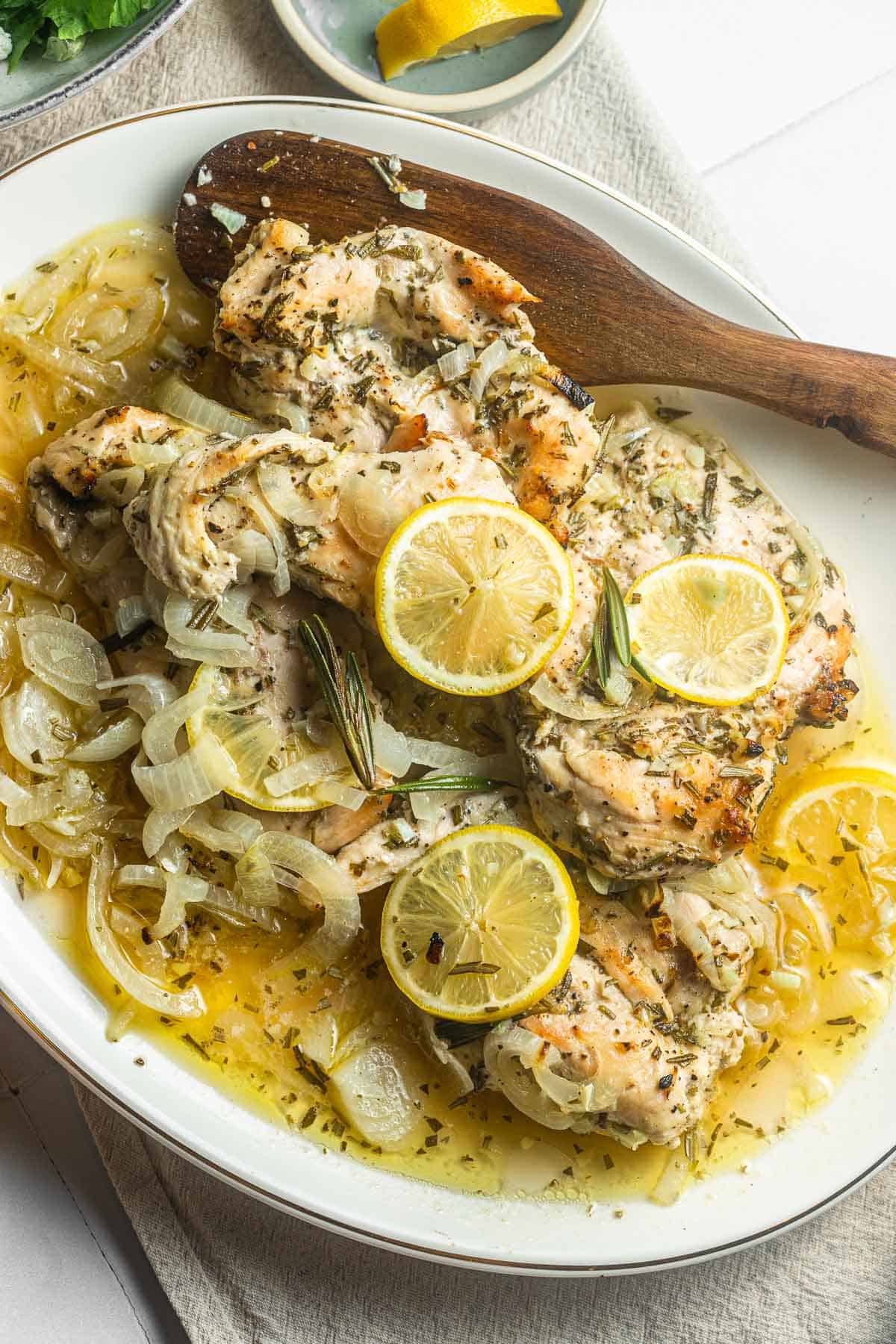 lemon rosemary chicken topped with lemon slices on a plate with a wooden spoon.