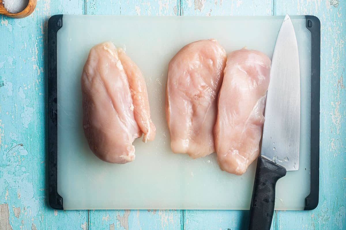 raw chicken breasts on a cutting board with a knife.
