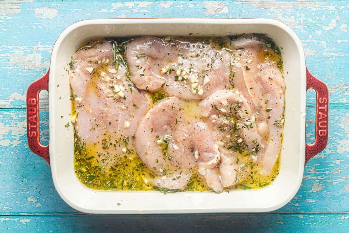 raw chicken breasts in a baking dish with olive oil, lemon juice, chicken broth, rosemary and minced garlic.
