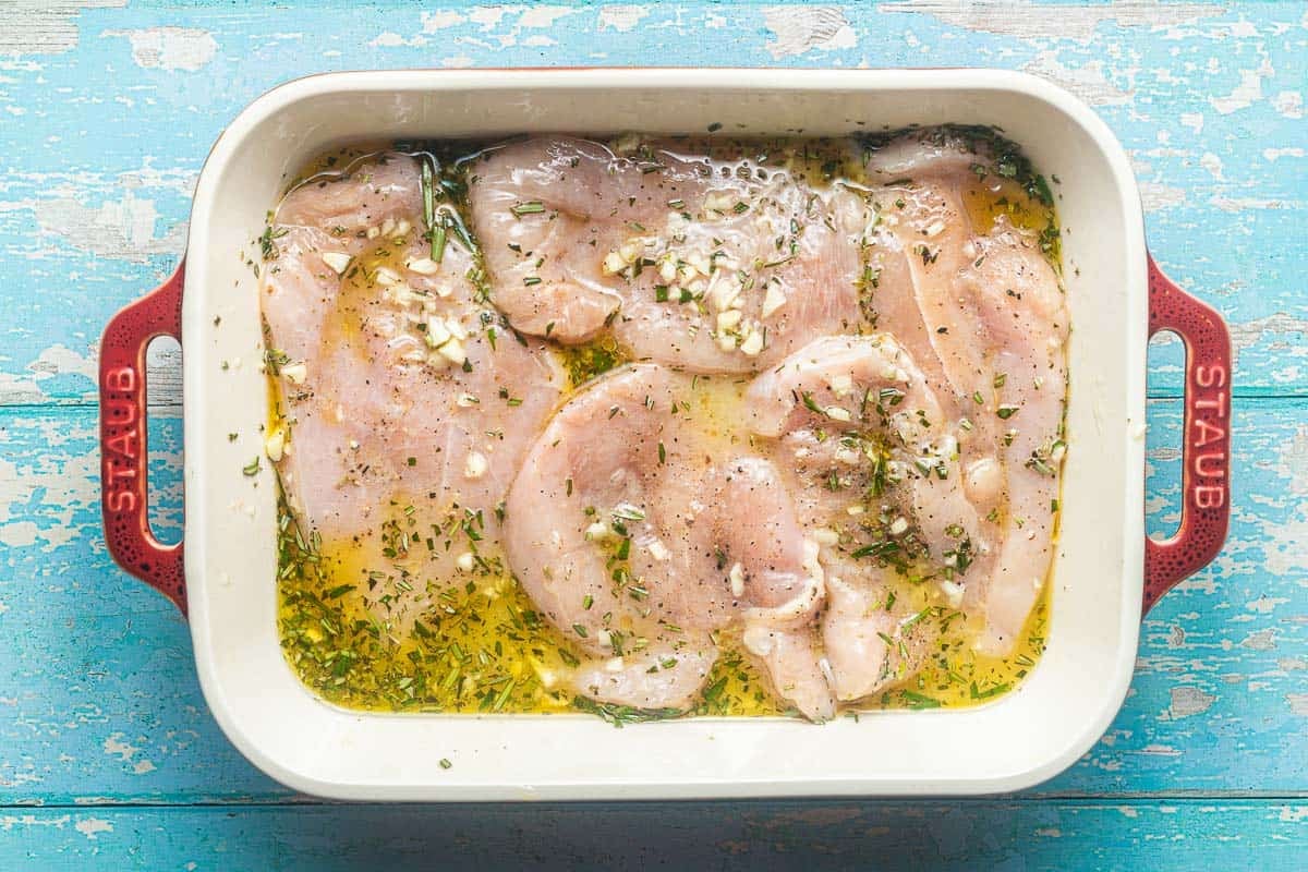 raw chicken breasts in a baking dish with olive oil, lemon juice, chicken broth, rosemary and minced garlic.