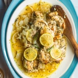 lemon rosemary chicken topped with lemon slices on a plate with a wooden spoon.