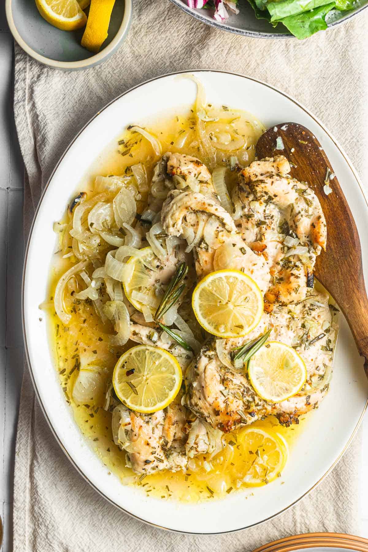 lemon rosemary chicken topped with lemon slices on a plate with a wooden spoon.