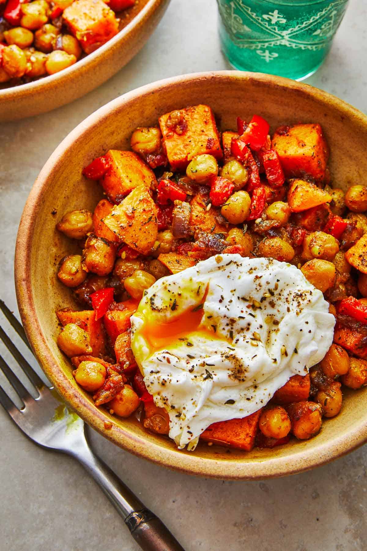close up of a bowl of sweet potato hash with a poached egg next to a fork.