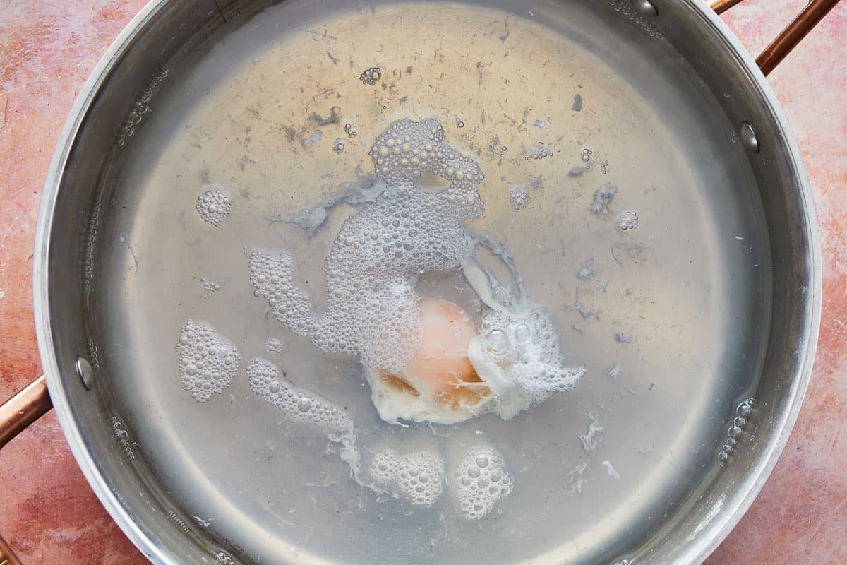 an egg being poached in a pan of boiling water.