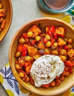two bowls of sweet potato hash with poached eggs next to a fork and a bowl of za'atar.