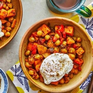 two bowls of sweet potato hash with poached eggs next to a fork and a bowl of za'atar.