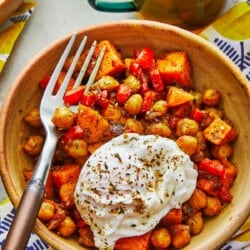 a bowl of sweet potato hash with a poached egg and a fork next to a mug of tea.