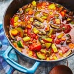 steamy homemade vegetable soup in a dutch oven next to a wooden spoon.