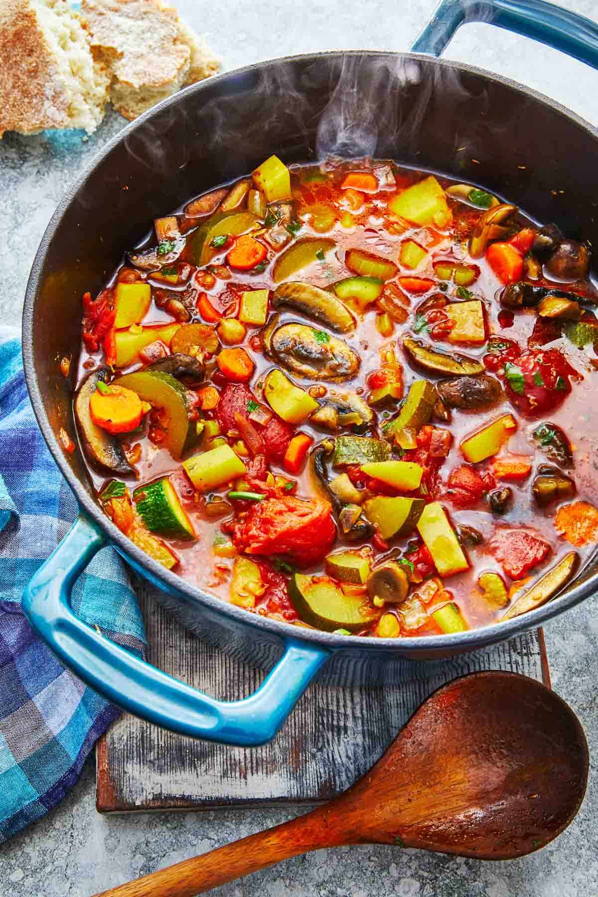 steamy homemade vegetable soup in a dutch oven next to a wooden spoon.